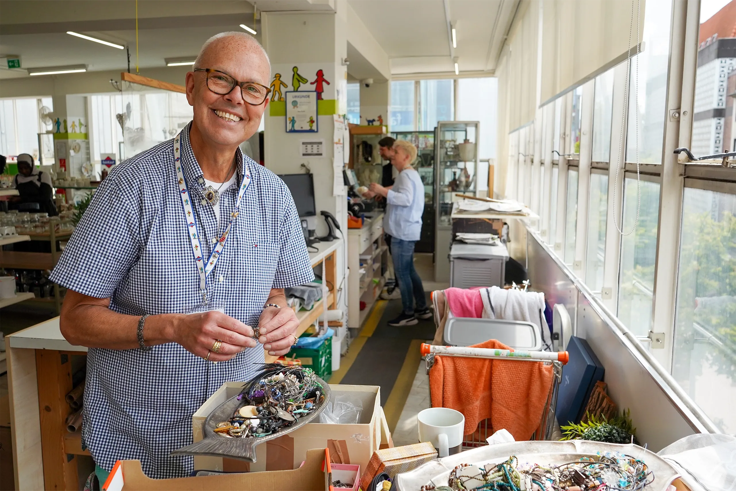 Älterer Mann sortiert Schmuck in einem Secondhandladen und lächelt in die Kamera.