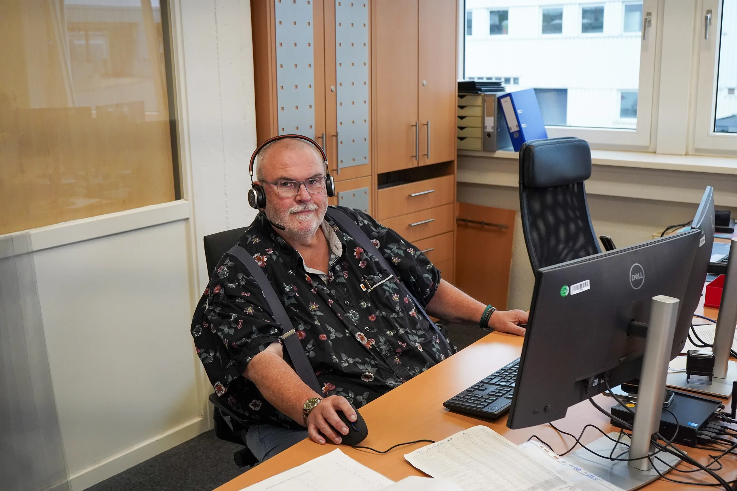 Mann in einem Büro sitzt am Schreibtisch vor einem Computer und trägt ein Headset.