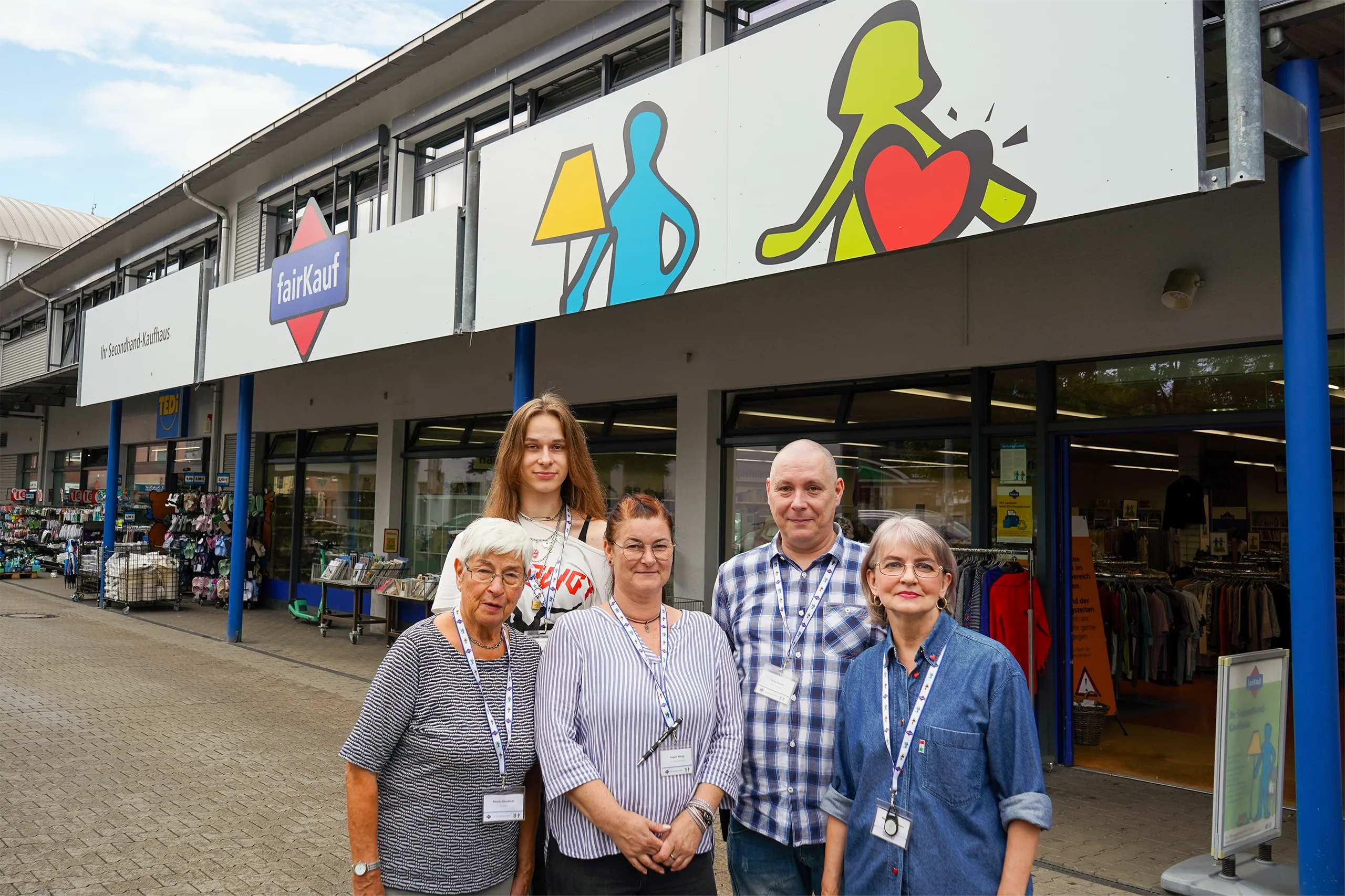 Fünf Mitarbeitende stehen vor einem fairKauf-Secondhandhaus mit Schaufenstern und Schild.