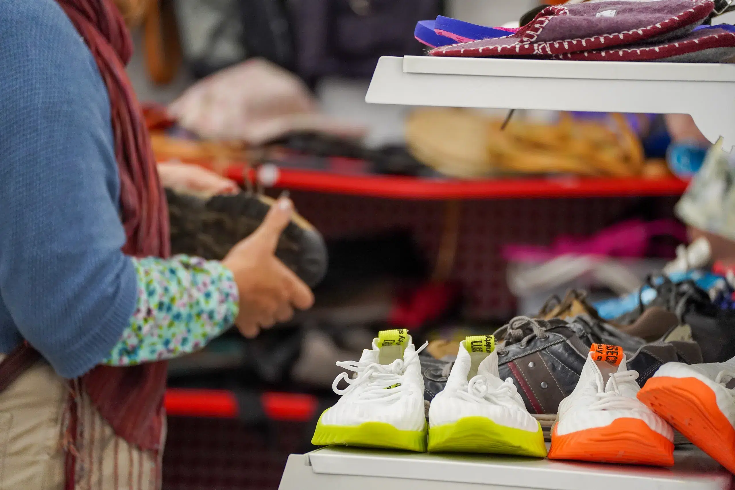 Person sortiert Schuhe in einem Secondhandladen; vorn stehen Sportschuhe in bunten Farben.