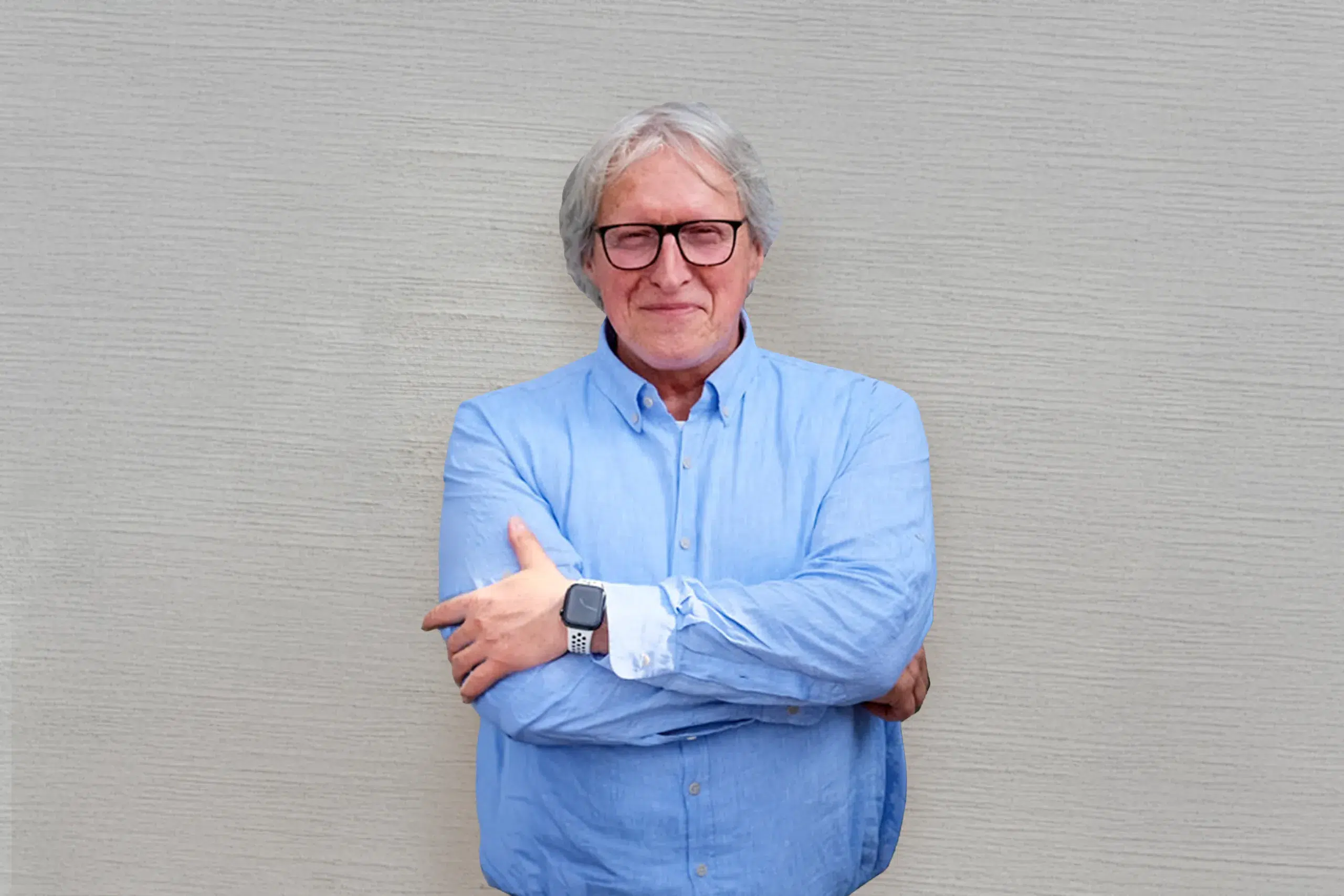 Mann mit Brille und blauem Hemd steht mit verschränkten Armen vor heller Strukturwand.