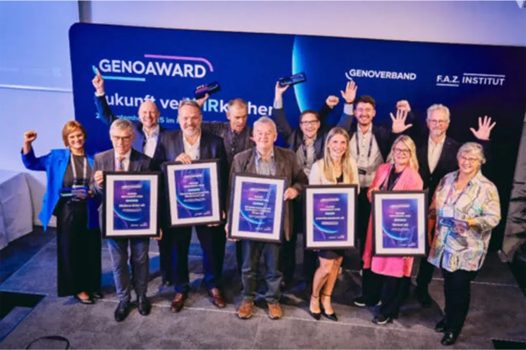 Gruppenfoto von zwölf Personen bei der Verleihung des GenoAwards, die stolz ihre Auszeichnungen halten und jubeln.