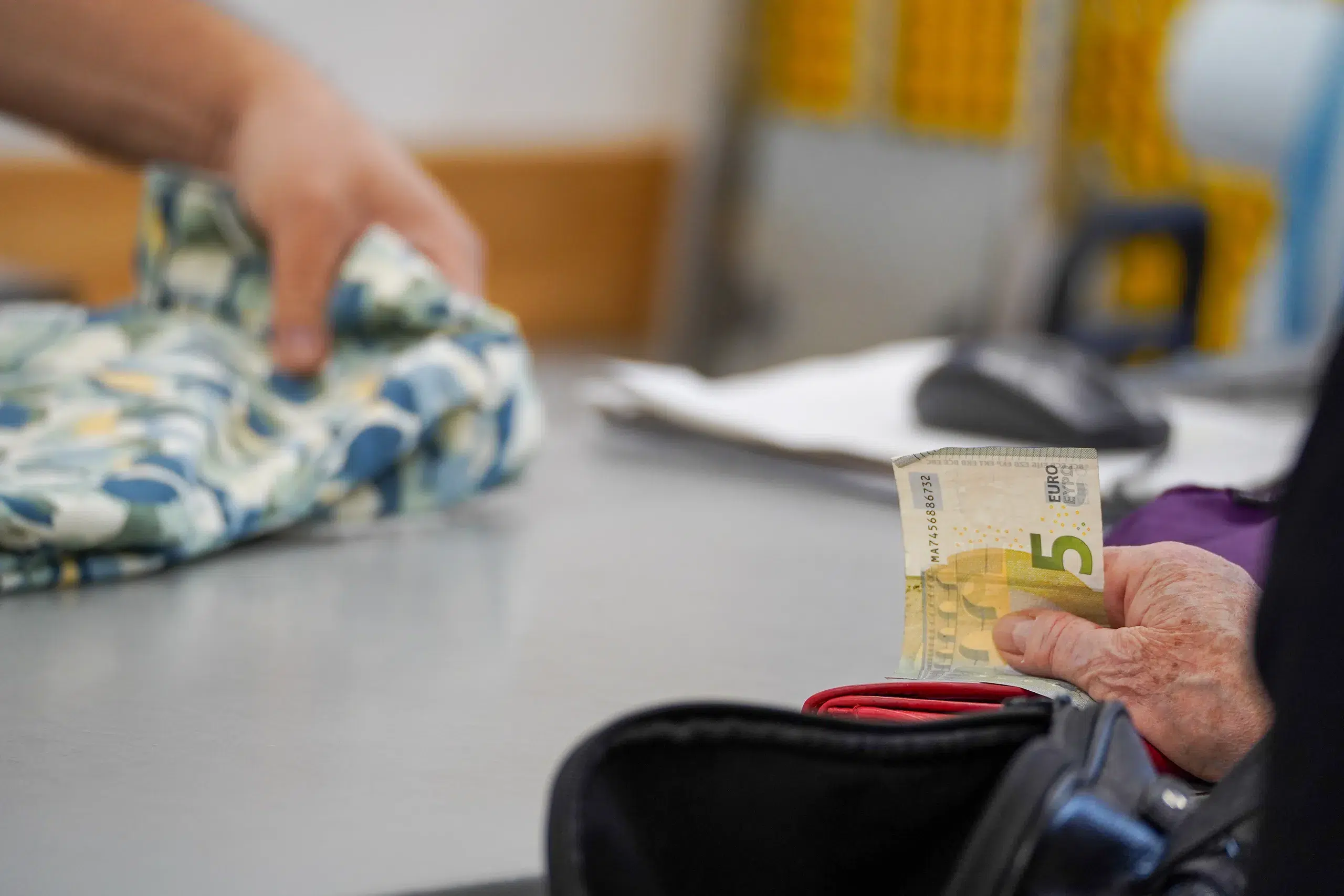 Kund*in bezahlt Kleidung im Secondhandladen mit einem Fünf-Euro-Schein.