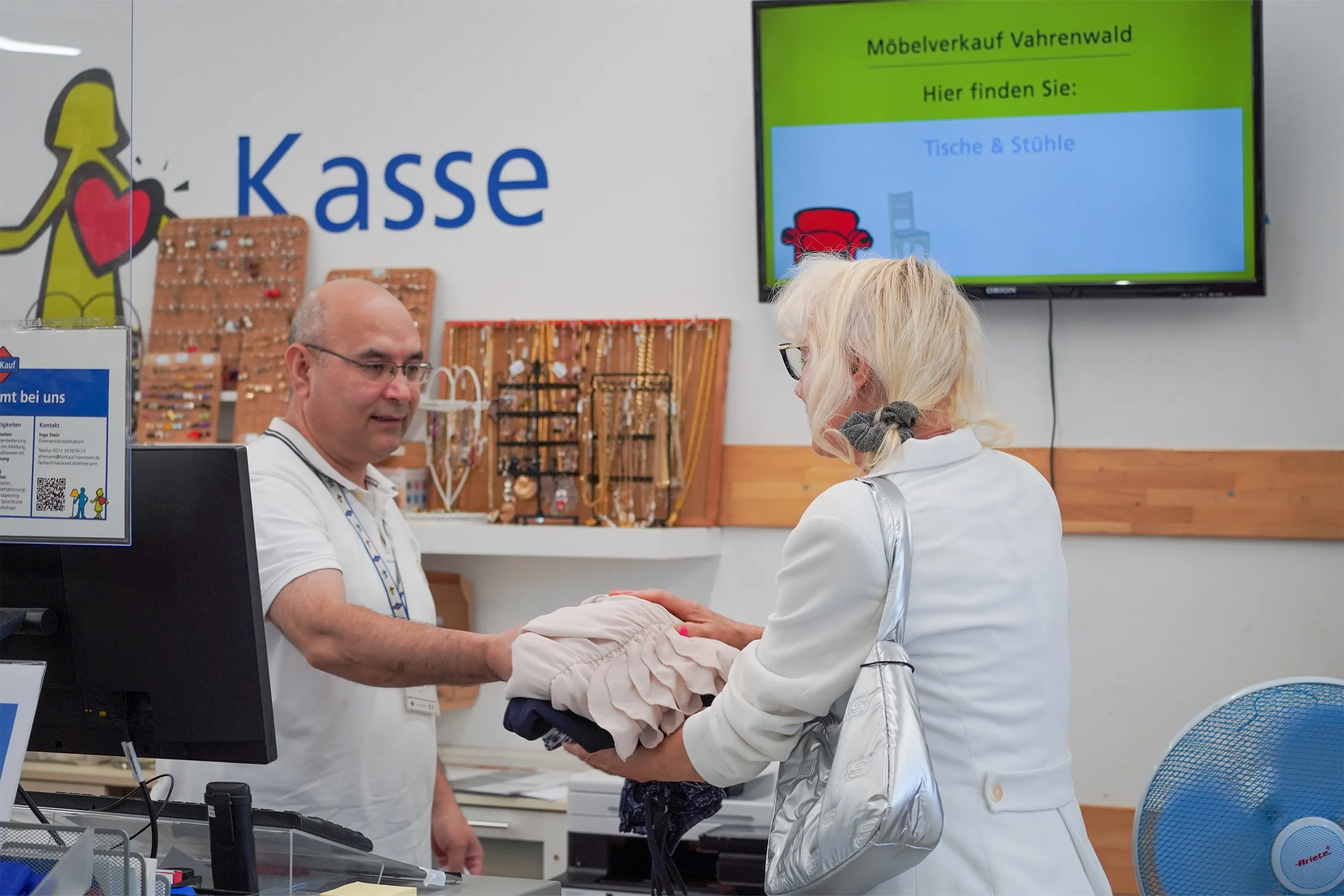 Eine blonde Frau übergibt einem Kassierer in einem Bekleidungsgeschäft mehrere Kleidungsstücke an der Kasse.