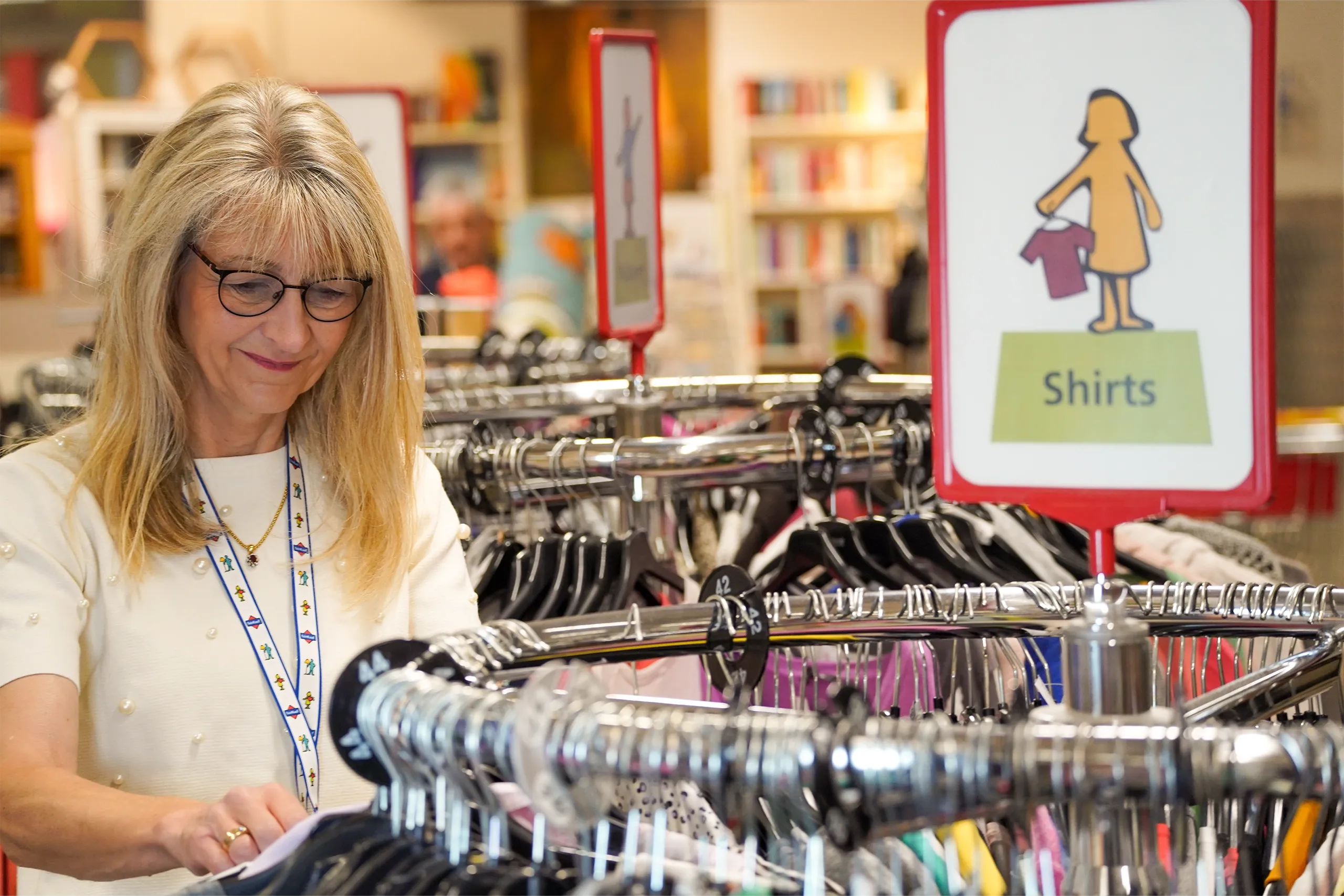 Eine Frau mit Brille sortiert T-Shirts in einem Bekleidungsgeschäft.