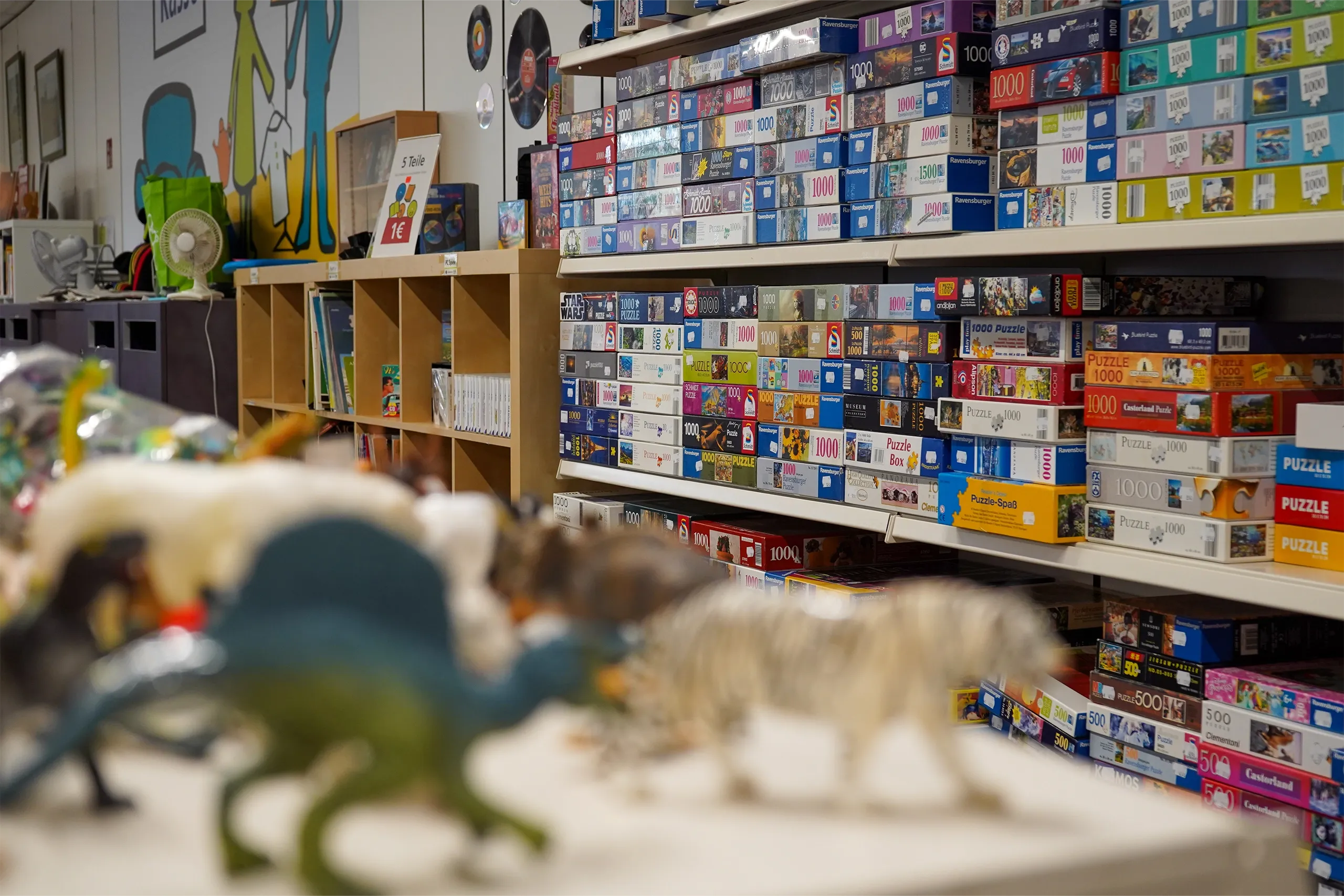 Regale voller Puzzle-Schachteln, vorn unscharfe Spielzeugtiere in einer Spielecke.