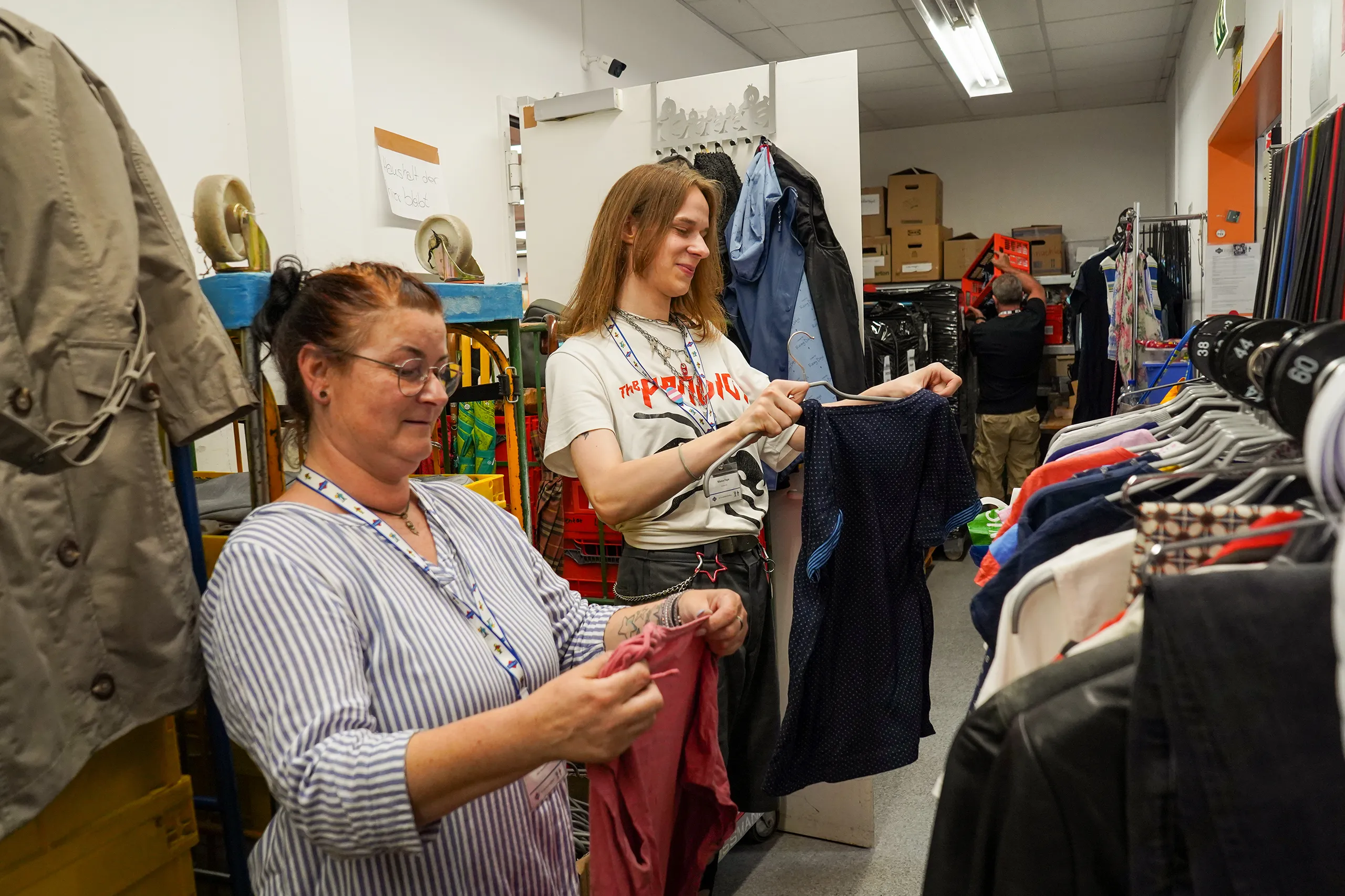 Zwei Personen in einem Bekleidungsgeschäft betrachten verschiedene Kleidungsstücke.