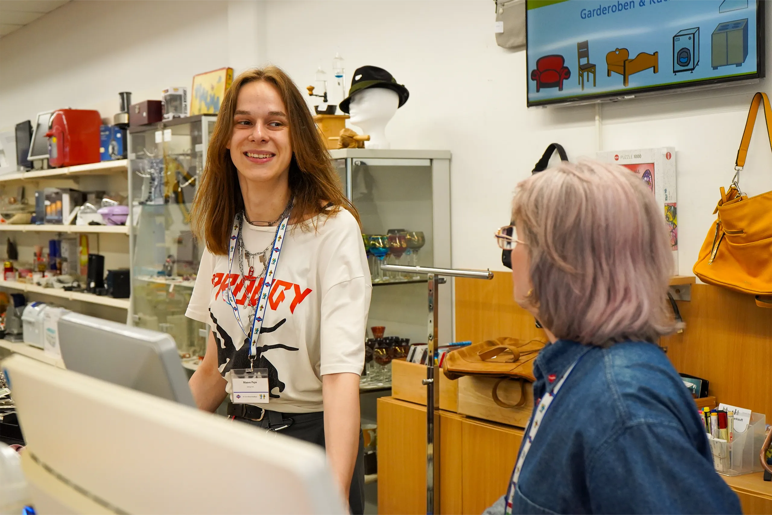 Zwei Mitarbeitende unterhalten sich lächelnd an der Kasse in einem Secondhandladen.