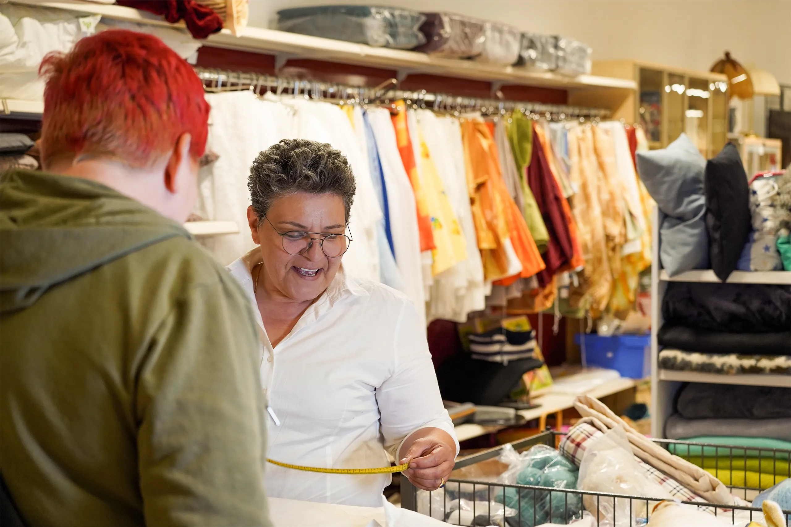 Mitarbeiterin misst Stoff ab und berät Kund*in im Secondhandladen.